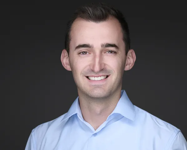 Headshot of a smiling man in a light blue shirt on a dark gray background
